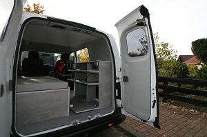 Einblick in den Microcamper durch die geöffneten Hecktüren. Auch die Türen sind mit grauem Stoff verkleidet. Stimmig dazu der grau gesprenkelte Fußboden. Die Dachverkleidung ist weiß, für einen hellen Innenraum.